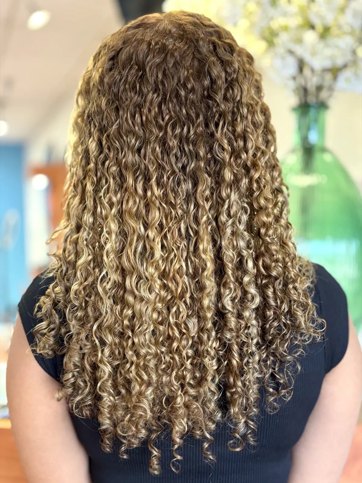 Long honey-blonde spiral curls with highlights, defined and frizz-free after a curly cut at Ciao Bella