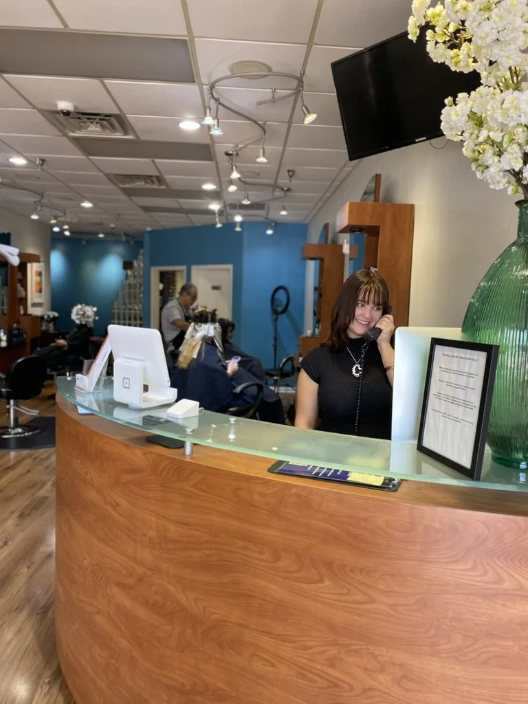 A Ciao Bella receptionist answering the phone at the front desk, salon floor behind