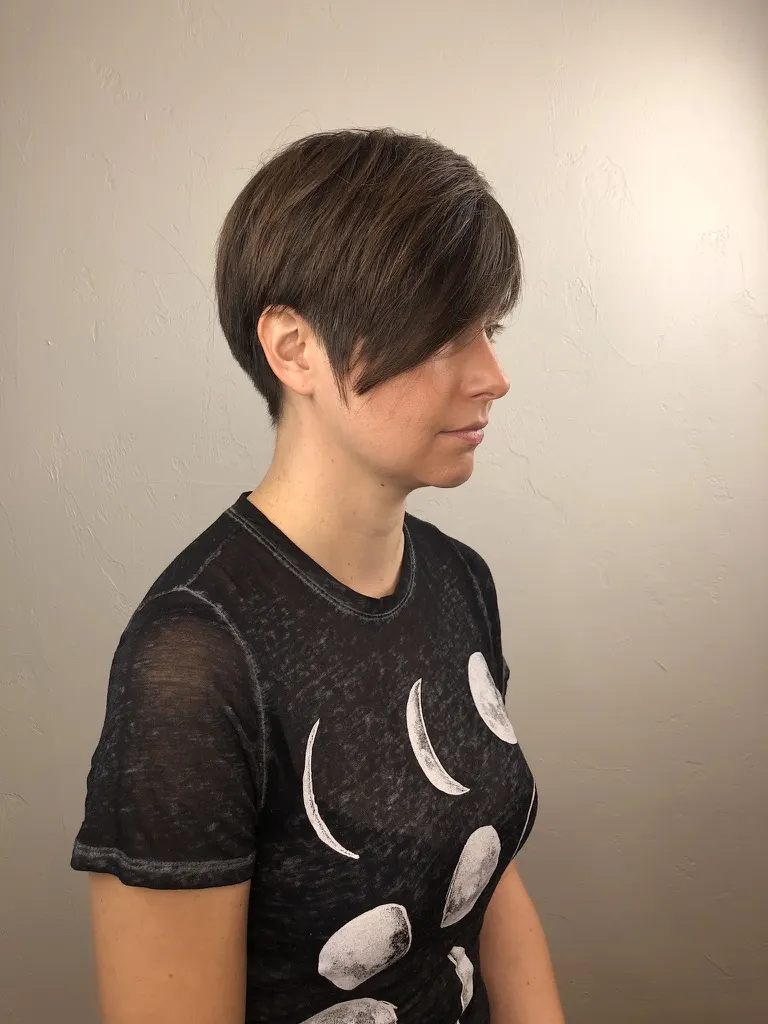 Side profile of a brunette pixie cut with a long swept fringe and a tapered, graduated nape