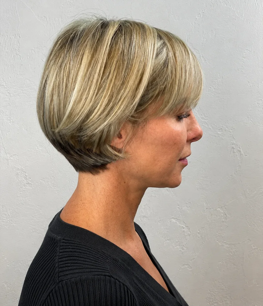 Jaw-length rounded blonde bob with a soft fringe and highlights, side profile