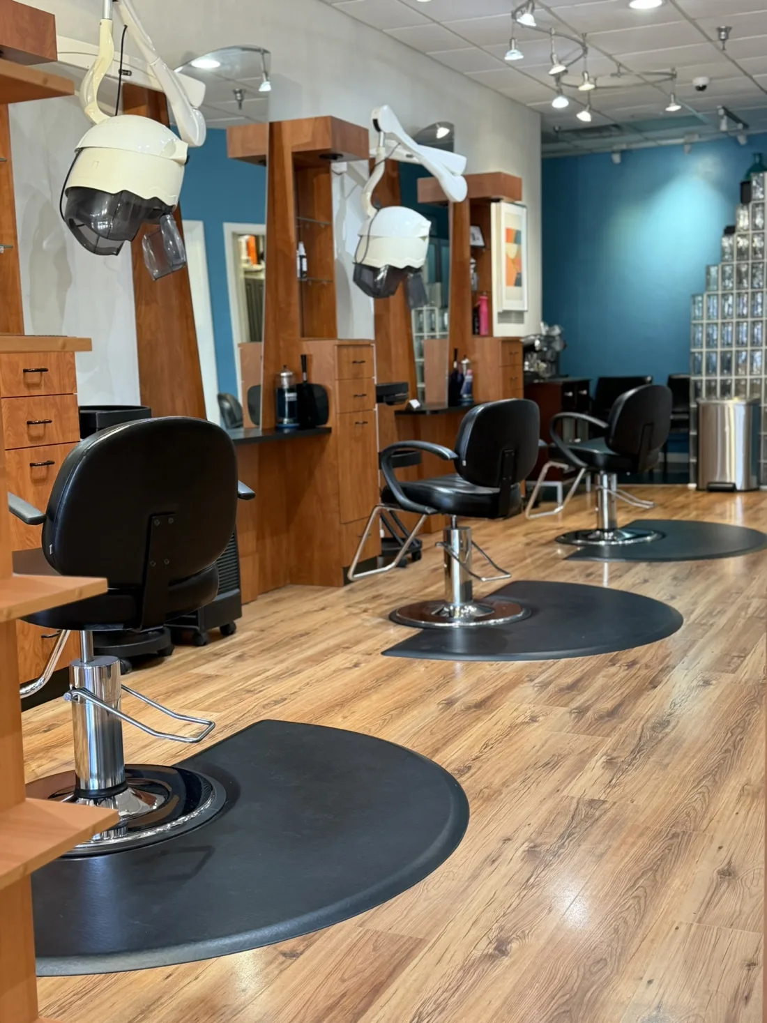Inside Ciao Bella Salon: a row of styling chairs, warm wood floors, and the teal accent wall