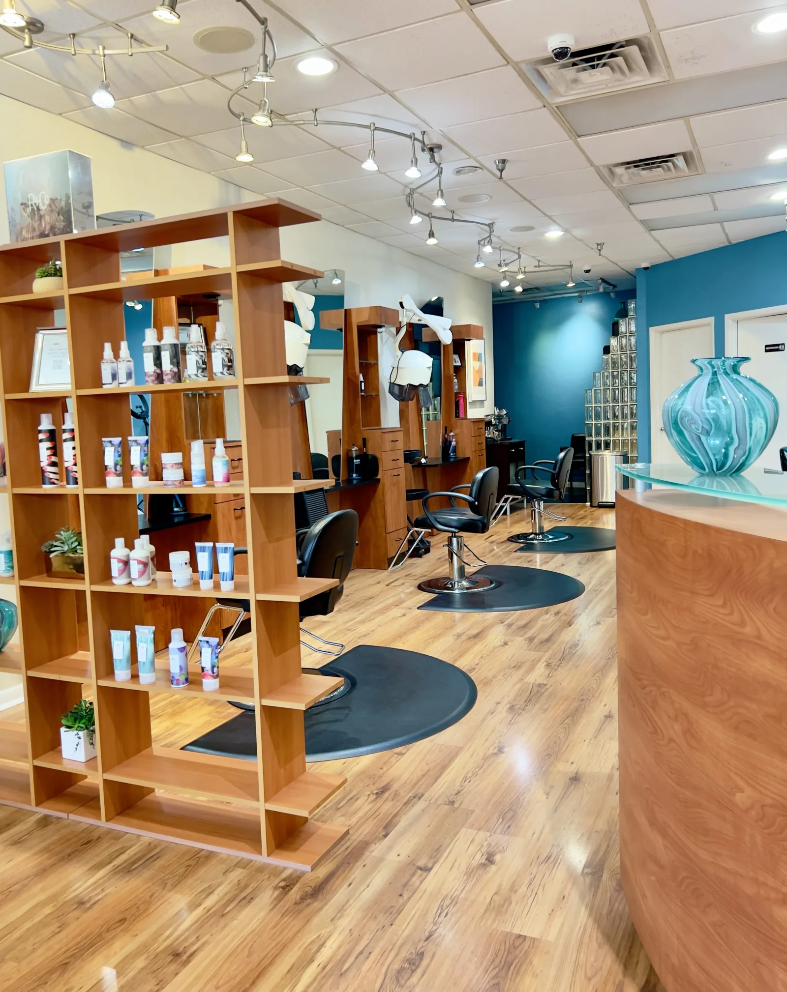 The Ciao Bella salon floor: styling chairs, R+Co product shelves, and the teal front desk