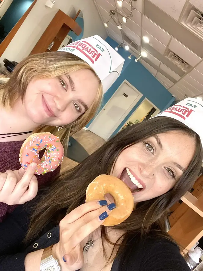 Two Ciao Bella team members in Krispy Kreme hats holding doughnuts in the salon